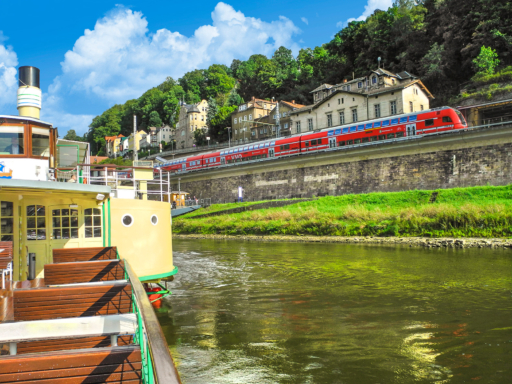 S-Bahn+SDS in Dampfer liegt in Königstein. Parallel dazu führt eine S-Bahn auf dem Bahndamm in Richtung Dresden. Es ist sonnig, ein paar weiße Wolken ziehen am Himmel.